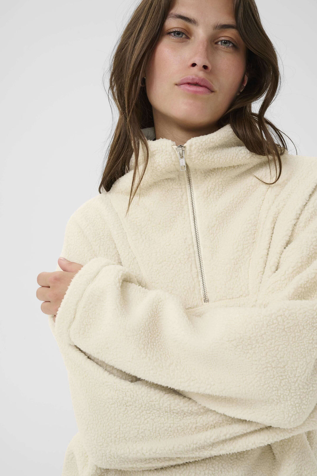 Femme portant un chandail Sirana en tissu sherpa, col montant zippé, couleur crème, style décontracté et confortable.