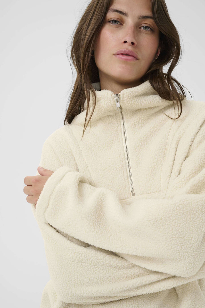 Femme portant un chandail Sirana en tissu sherpa, col montant zippé, couleur crème, style décontracté et confortable.