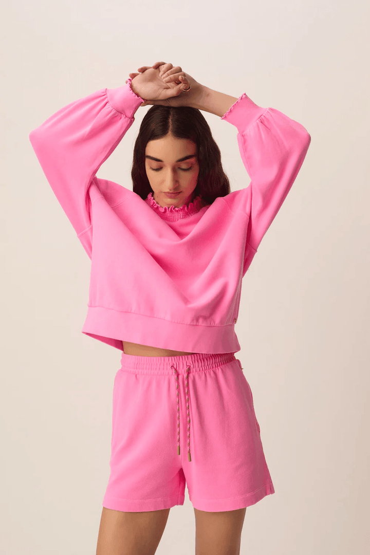 Chandail Yaelle ouaté court à manches longues coupe ample rose porté par une femme avec shorts assortis.