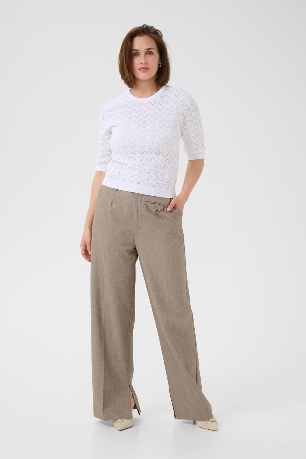 Chandail ajouré blanc à col rond, porté avec un pantalon beige, pour une tenue chic et féminine.