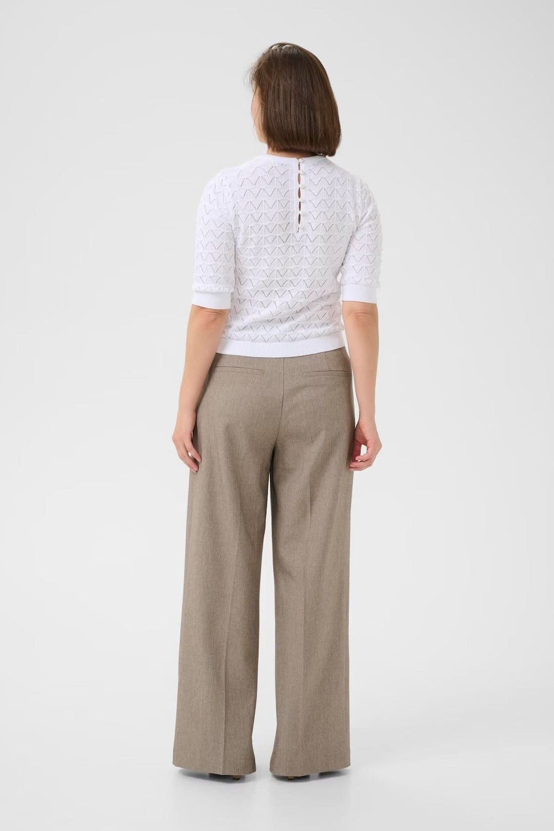 Chandail ajouré blanc avec boutons perlés à l'arrière, porté avec un pantalon large beige.
