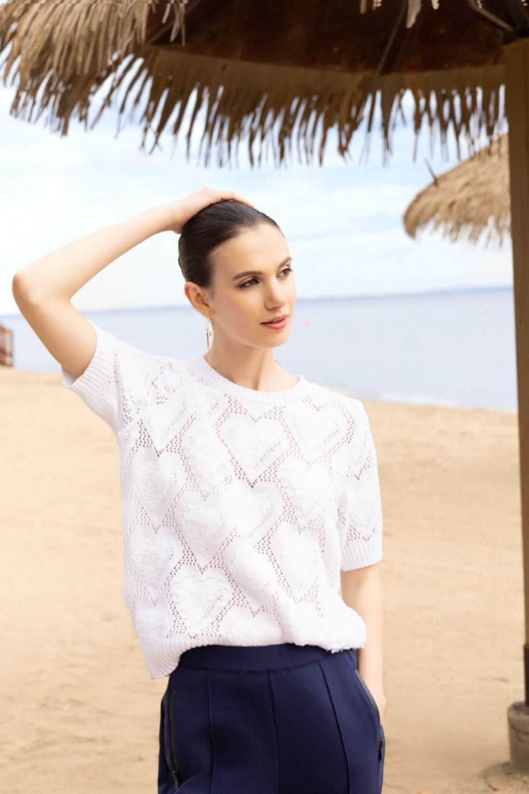 Femme sur la plage portant un chandail ajouré à motif cœur, léger et féminin, avec une encolure ronde et manches courtes.