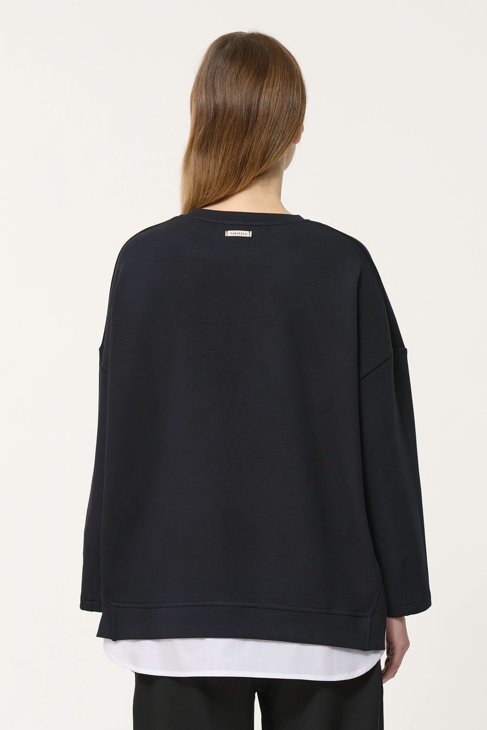 Vue arrière d'un chandail ample noir au style minimaliste avec superposition blanche.