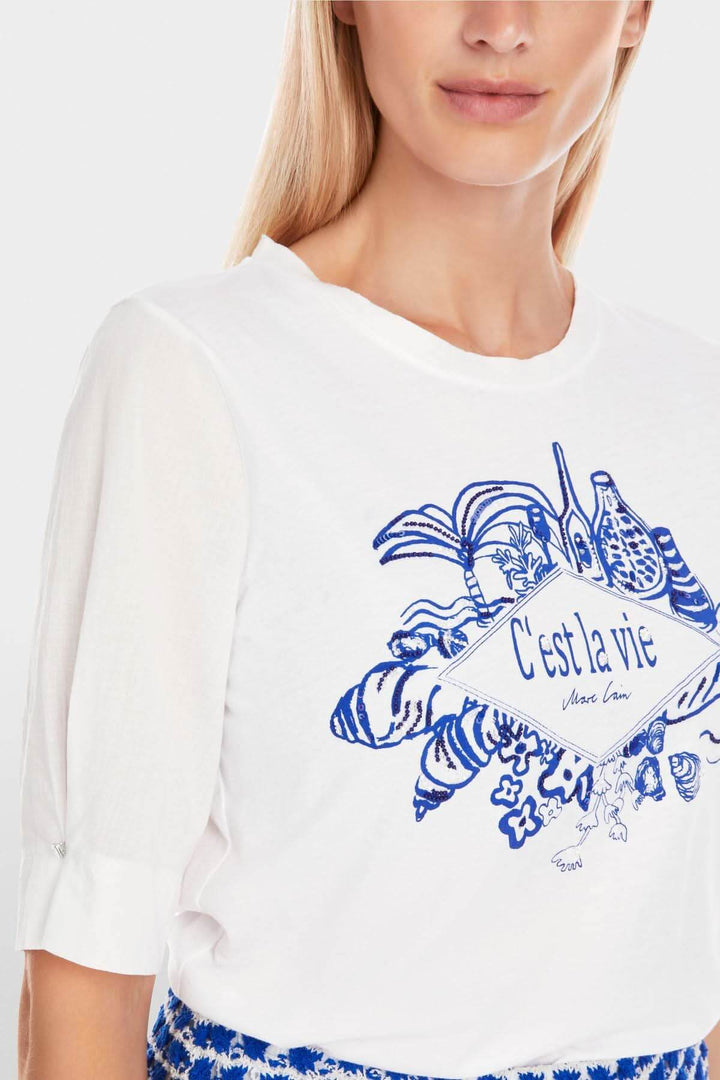 Chandail blanc avec écriture 'C'est la vie' et illustration colorée, à porter pour un look estival chic.
