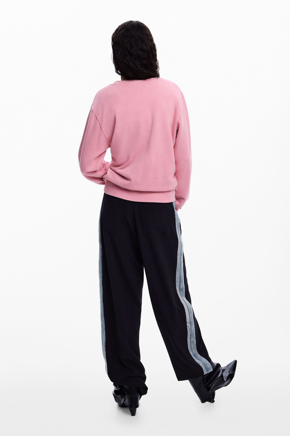 Homme portant un chandail rose avec logo et perles, vue arrière, coupe décontractée, manches longues, look moderne et créatif.