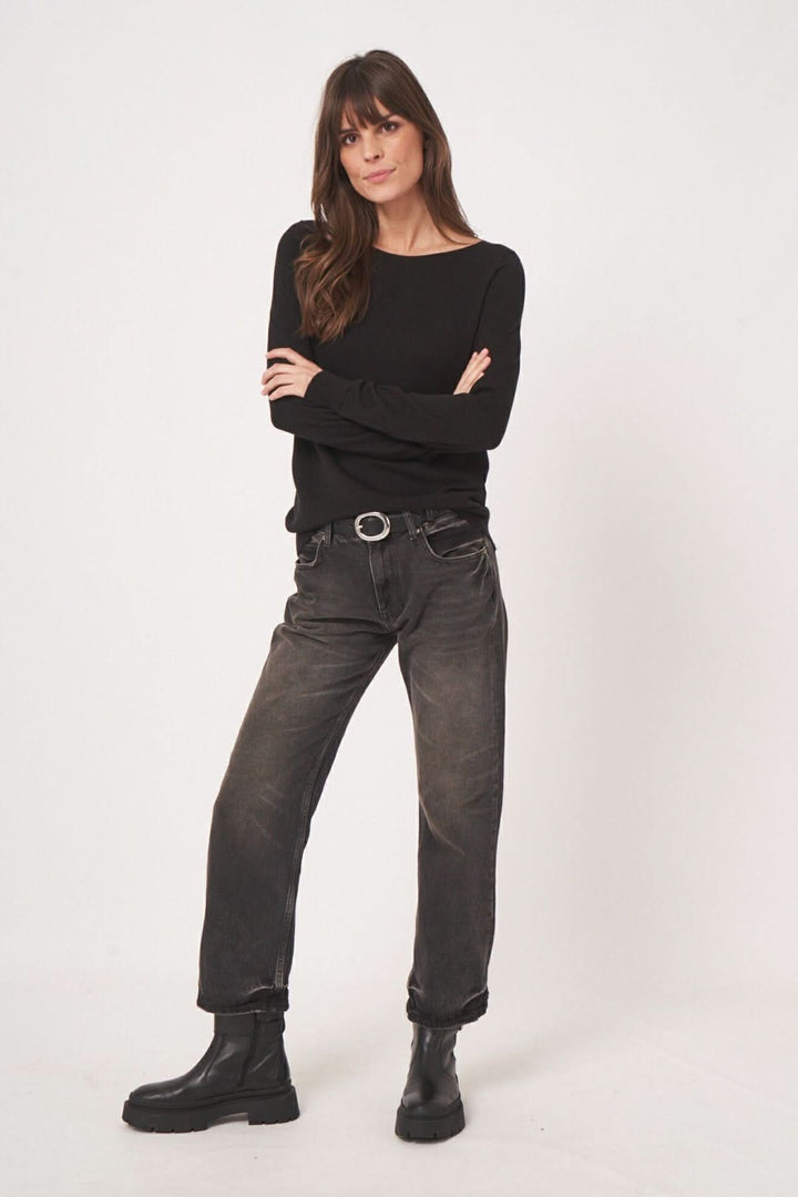Femme portant un chandail basique à encolure bateau et un jean noir, affichant un look minimaliste et élégant.