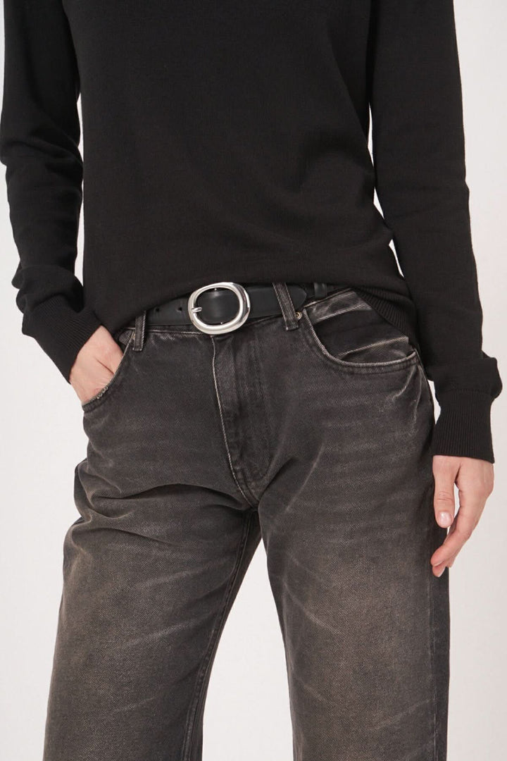 Chandail basique noir à encolure bateau avec ceinture en métal et jean délavé pour un look minimaliste.