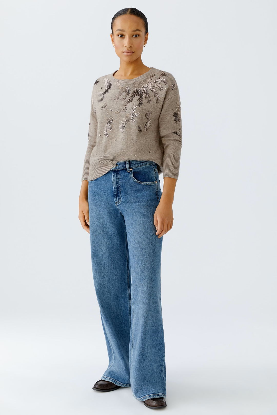 Femme portant un chandail broderies beige avec un jean, illustrant le design élégant et festif du vêtement.