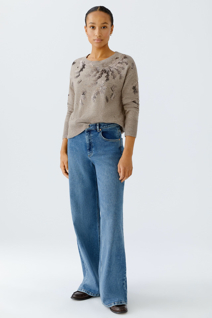 Femme portant un chandail broderies beige avec un jean, illustrant le design élégant et festif du vêtement.