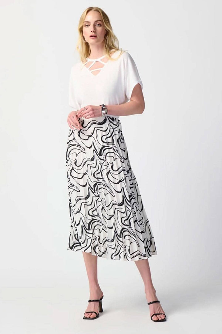 Femme portant un chandail col en V avec un détail découpé, associé à une jupe à motifs ondulés noirs et blancs.