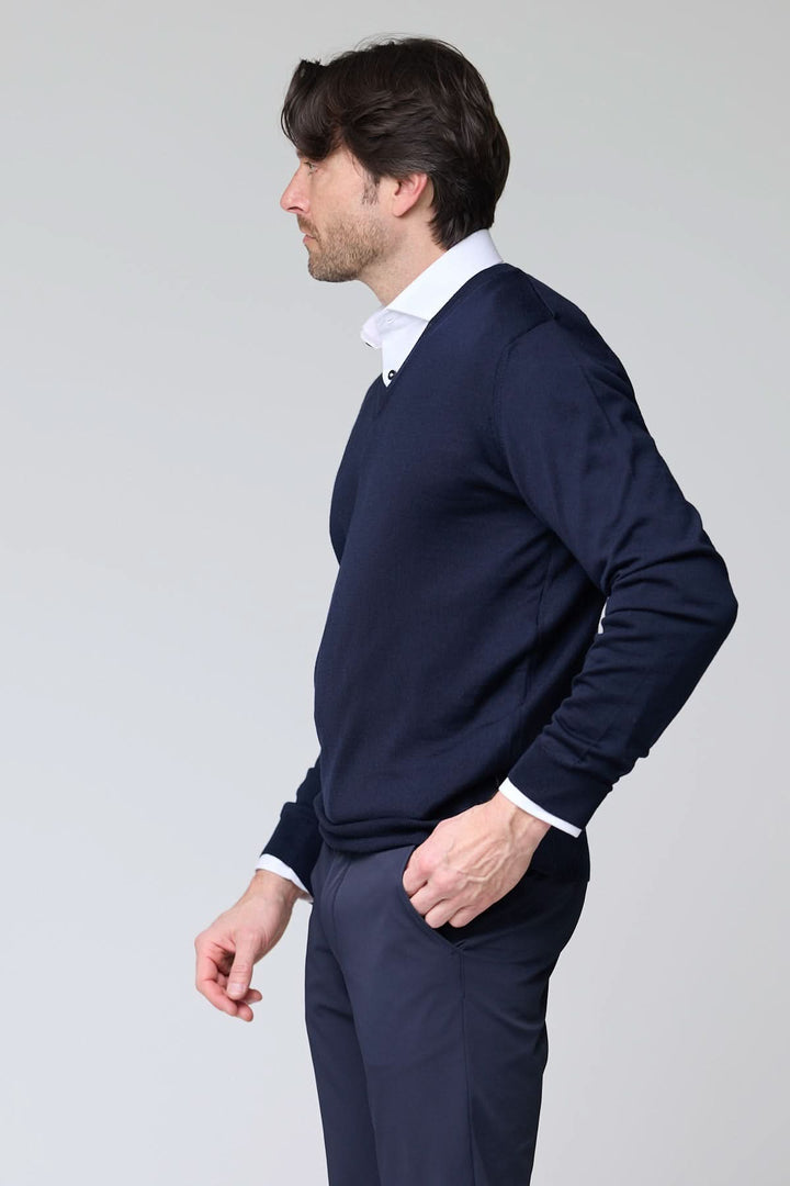 Homme portant un chandail col en V en laine mérinos bleu marine, élégant sur une chemise blanche, style intemporel.