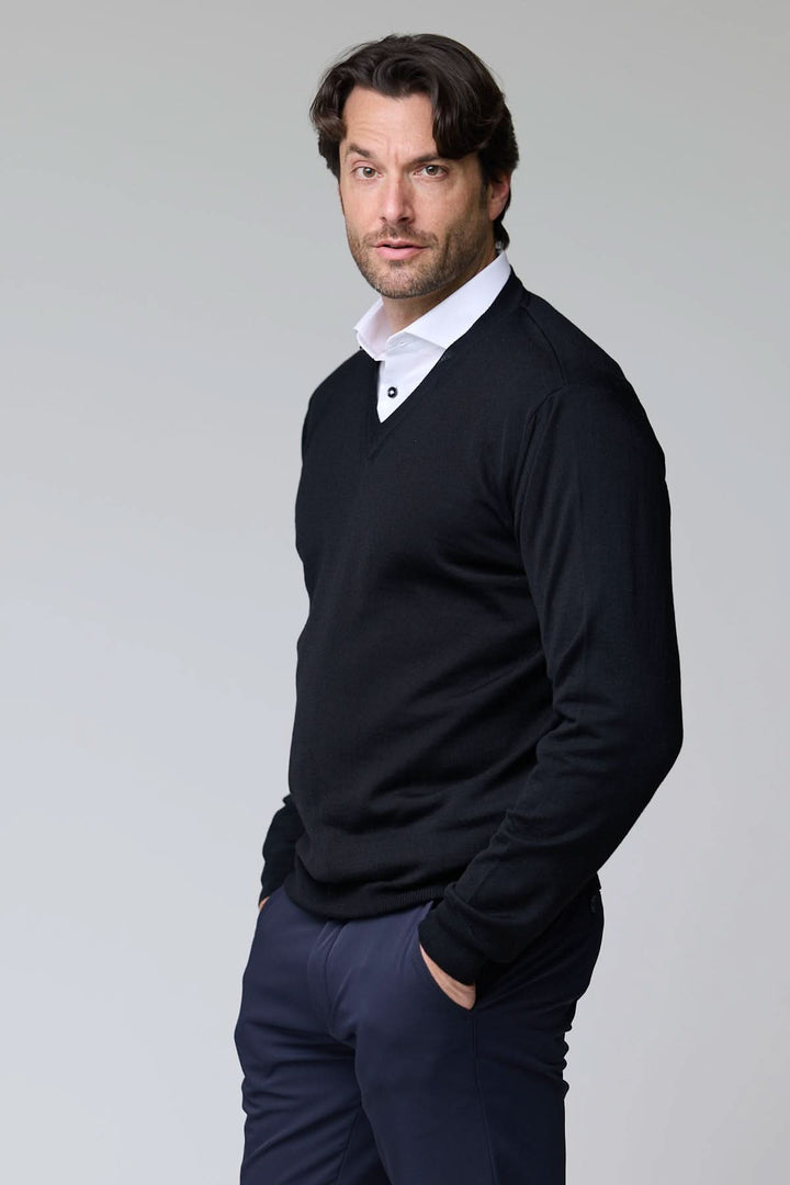 Homme portant un chandail col en V en laine mérinos noire élégant, sur une chemise blanche, style classique et intemporel.