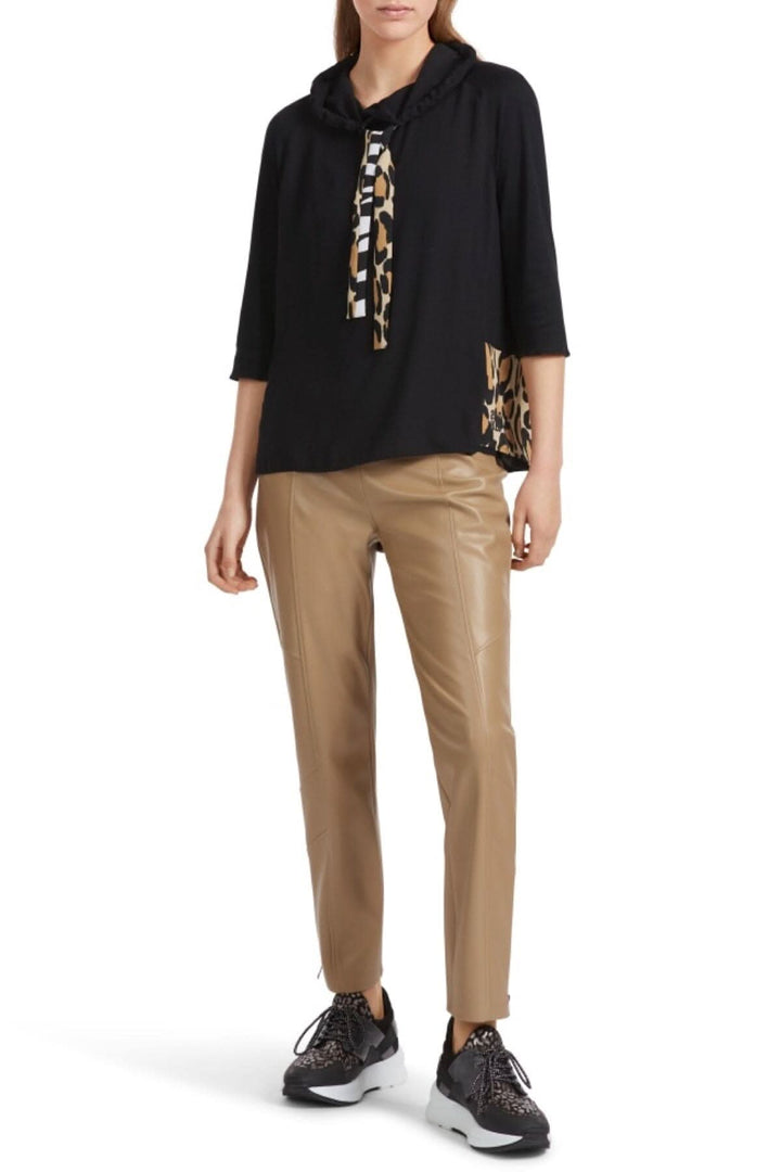 Chandail col montant noir avec manches raglan, cordon de serrage, et motif animalier sur le côté, porté avec un pantalon beige.