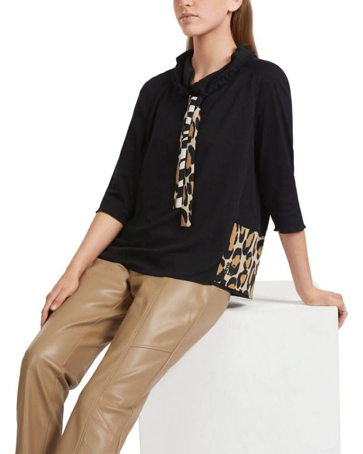 Chandail col montant noir avec détail animalier et manches raglan, porté avec un pantalon en cuir.