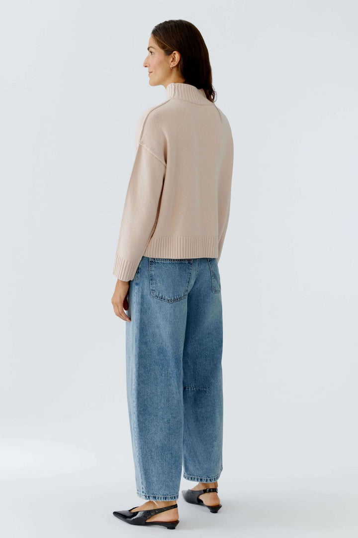 Femme portant un chandail à col montant en maille douce beige avec un jean ample, vue arrière.