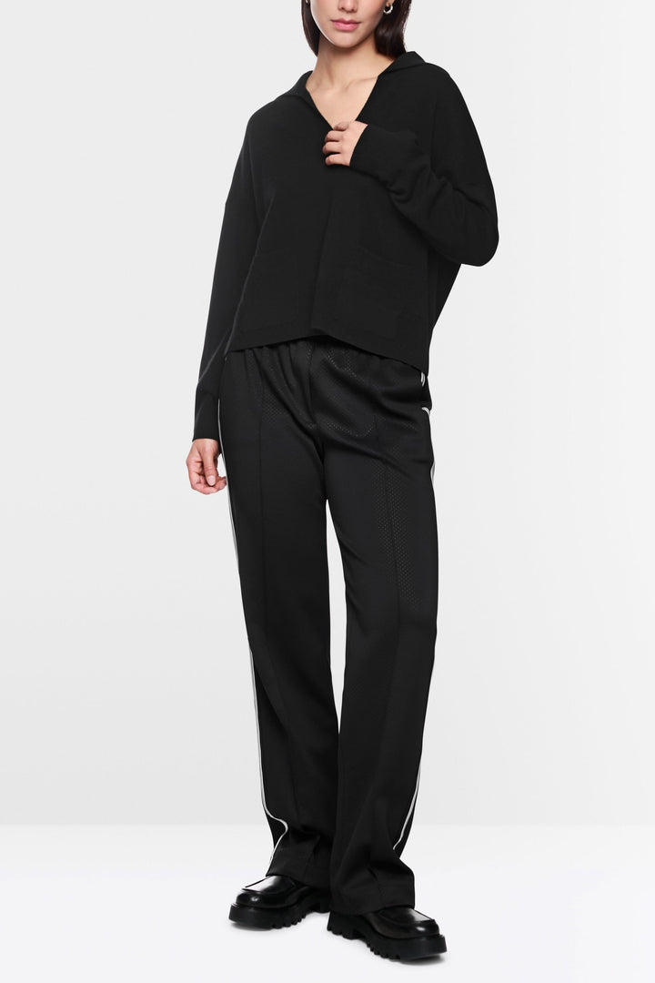 Chandail col ouvert noir en maille douce, porté avec un pantalon noir pour un look décontracté et élégant.