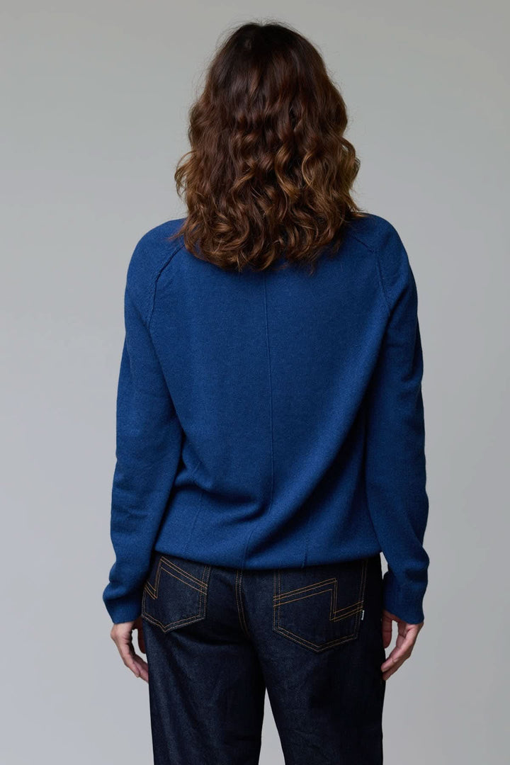 Vue arrière d'une femme portant un chandail à col rond bleu avec coupe classique, manches longues et détails côtelés.