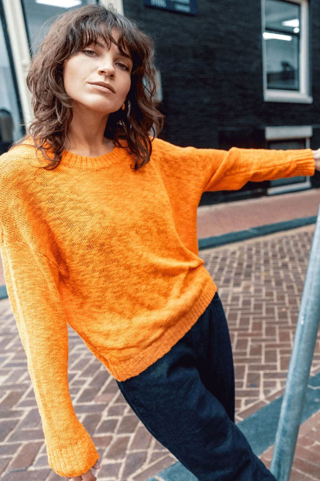 Chandail à col rond en coton bio, coupe décontractée et texture en relief, coloris orange vibrant, porté en extérieur.