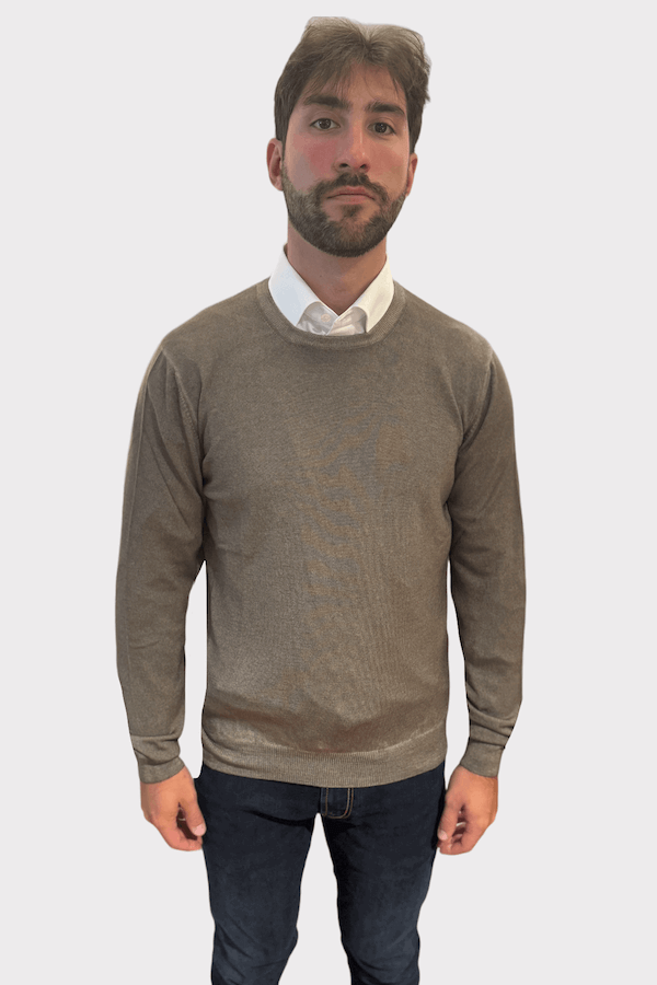 Homme portant un chandail col rond en laine gris, associé à une chemise blanche et un jean.