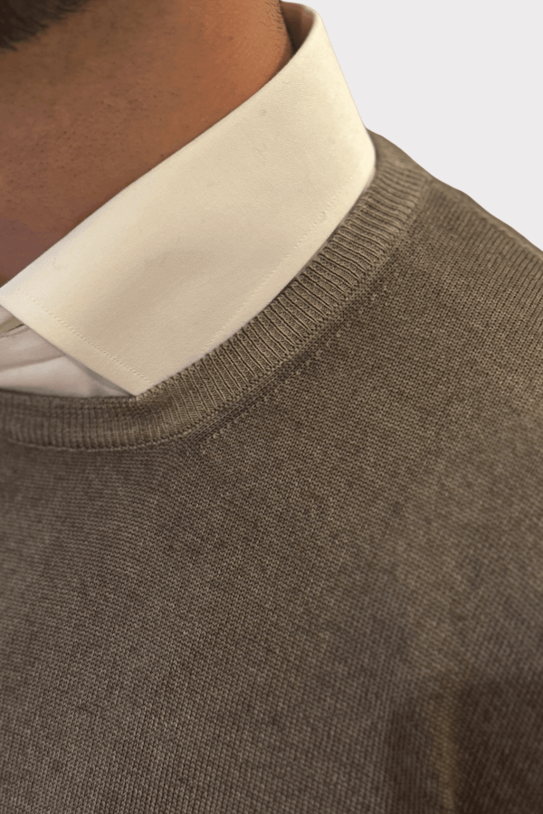 Détail d'un chandail col rond en laine porté sur une chemise blanche.
