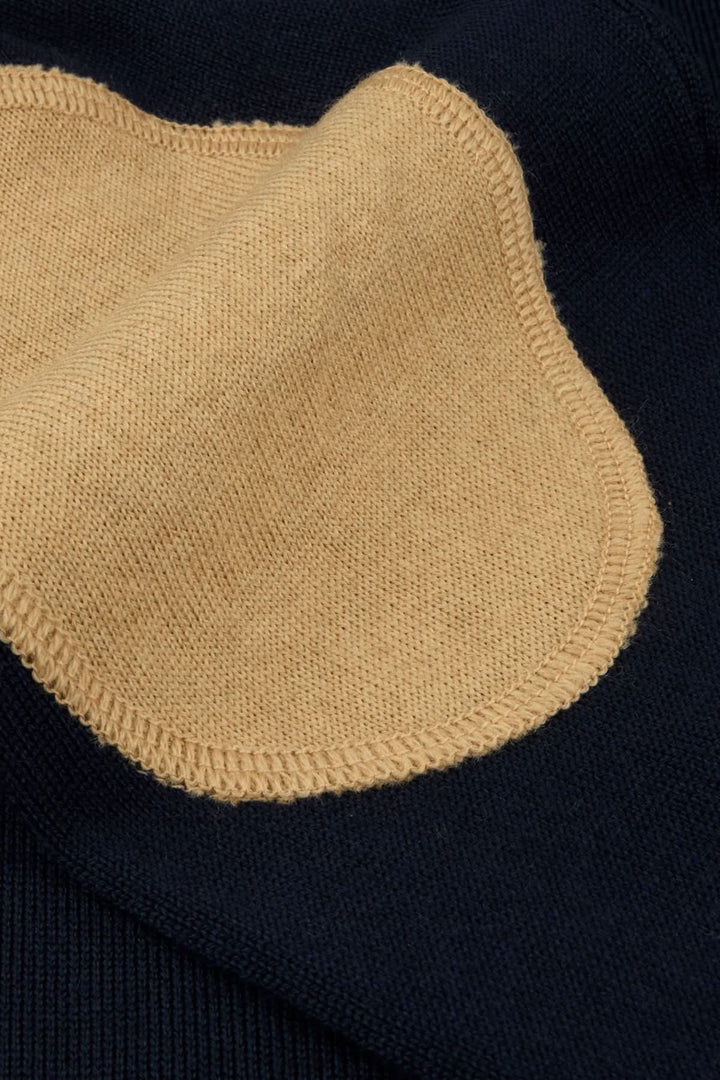 Chandail col rond en laine mérinos avec coudes contrastants, gros plan sur coudières intégrées beige sur fond bleu marine.