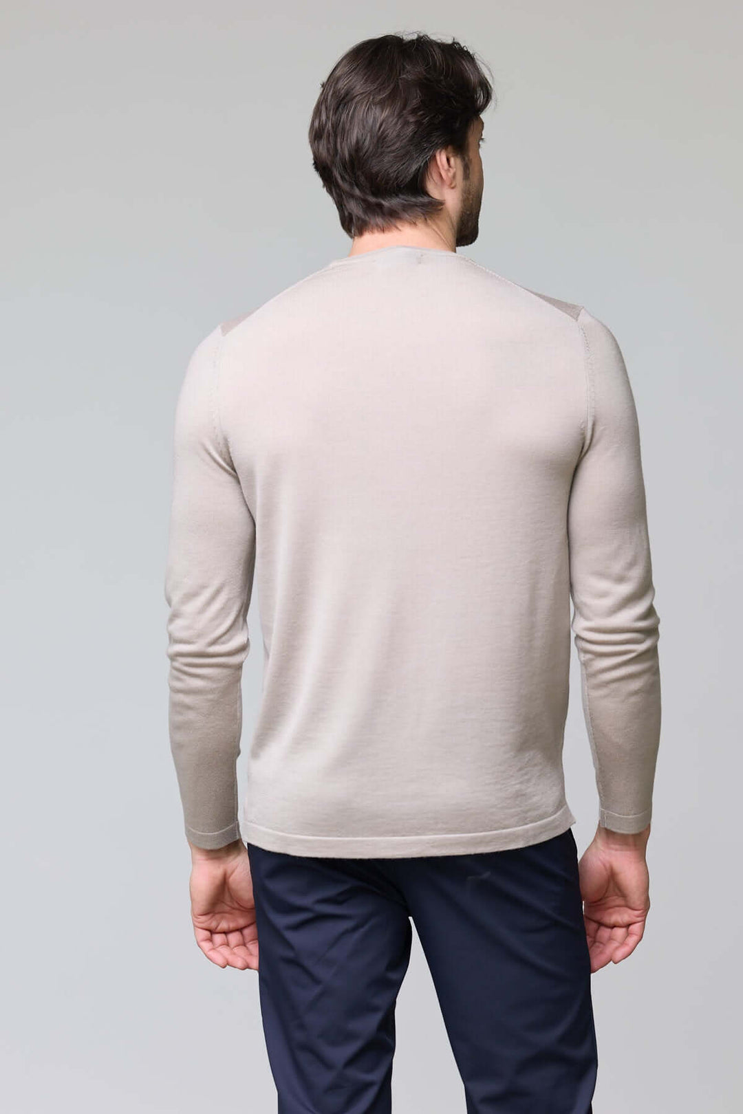 Homme portant un chandail col rond en tricot fin beige à manches longues, vu de dos, avec un pantalon bleu.