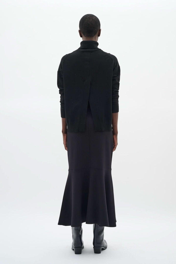 Chandail à col roulé noir avec coupe décontractée, porté avec une jupe longue pour un look chic.