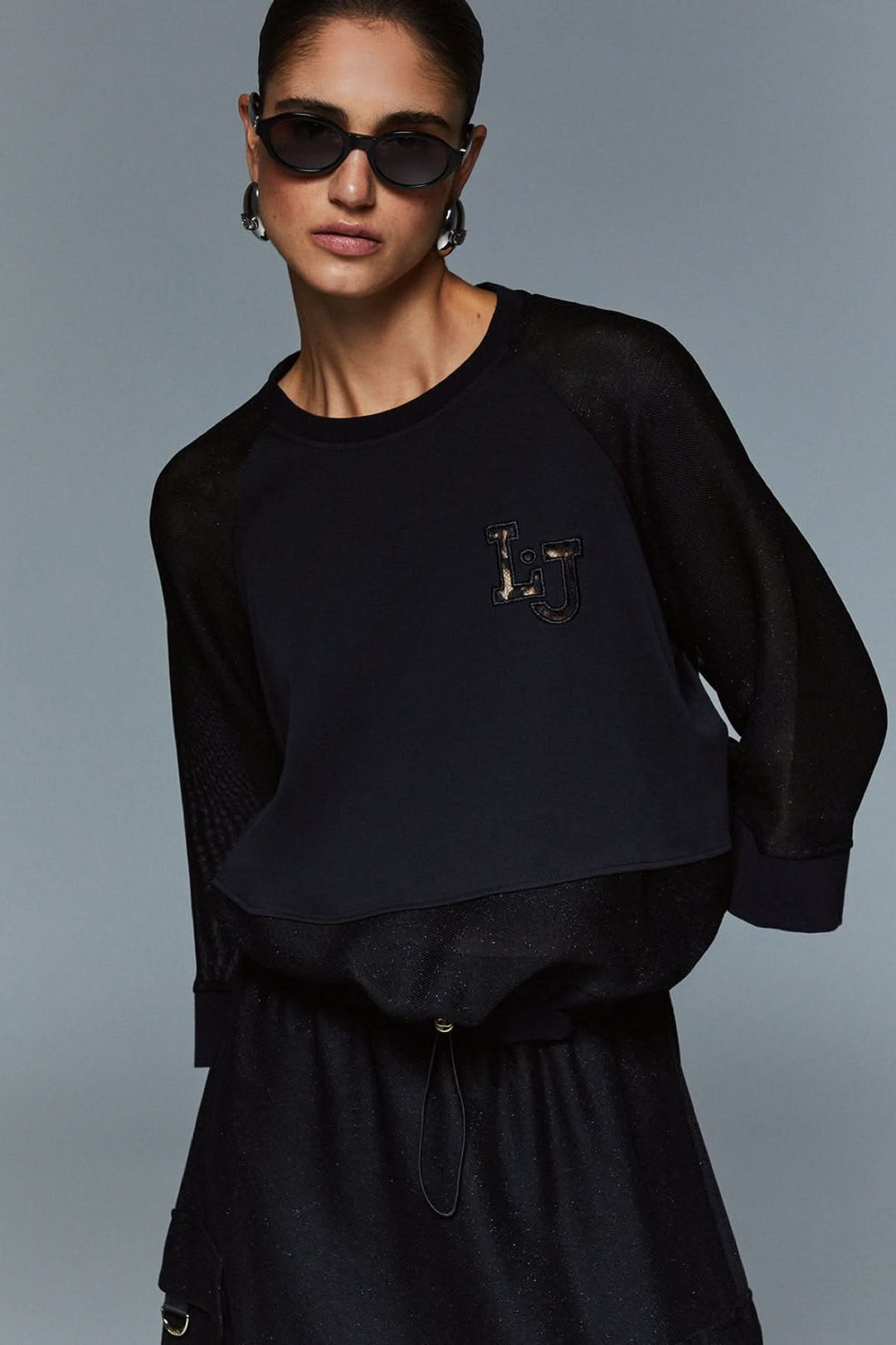 Chandail court à manches larges avec style sportif et féminin, coupe ample, manches trois-quarts, écusson logo, allure moderne.