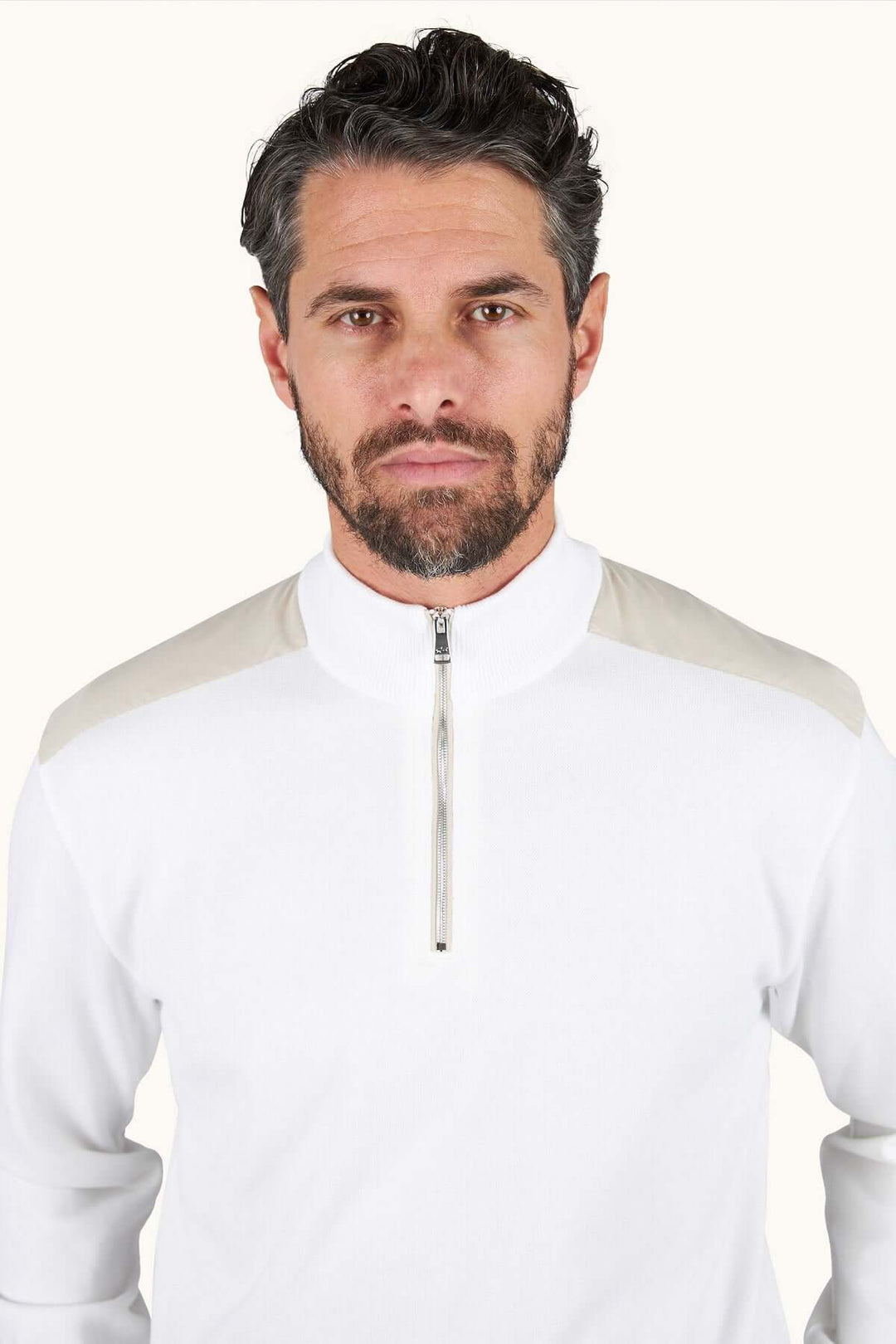 Homme portant un chandail à demi-zip blanc, style décontracté chic avec col montant et silhouette moderne.