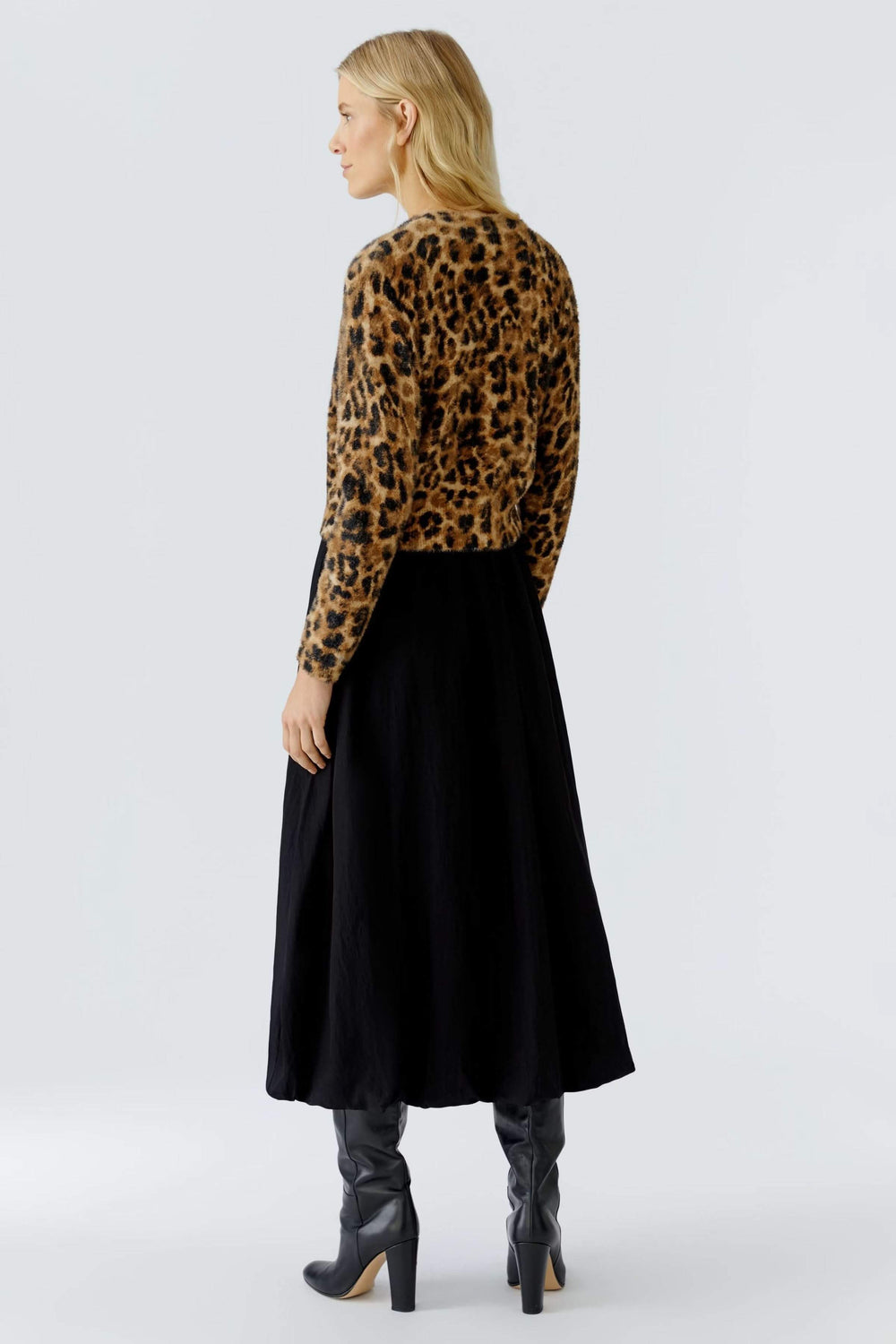 Femme portant un chandail duveteux à motif animal avec jupe noire et bottes élégantes, vue de dos.