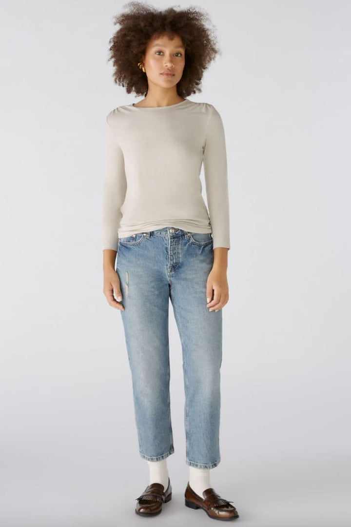 Chandail long beige à manches, porté avec un jean bleu, style décontracté et élégant.