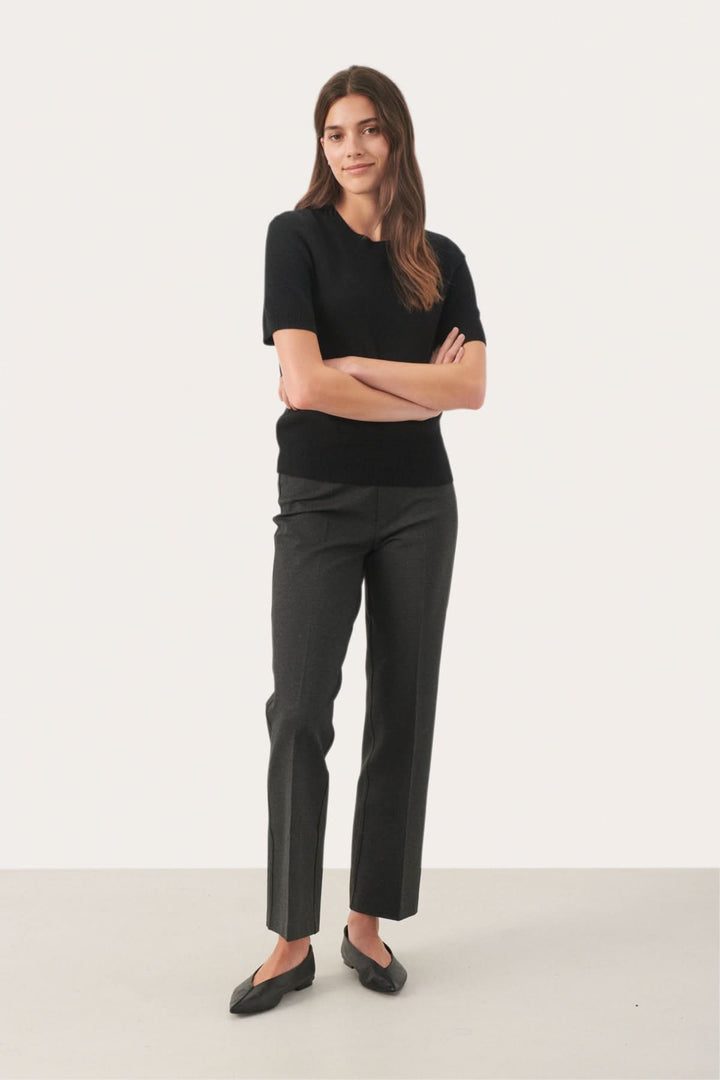 Femme portant un chandail en cachemire noir à manches courtes et un pantalon gris, style élégant et moderne.