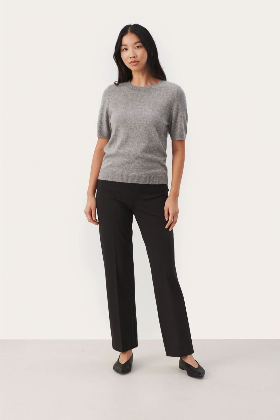 Chandail en cachemire gris à manches courtes, porté avec un pantalon noir élégant.