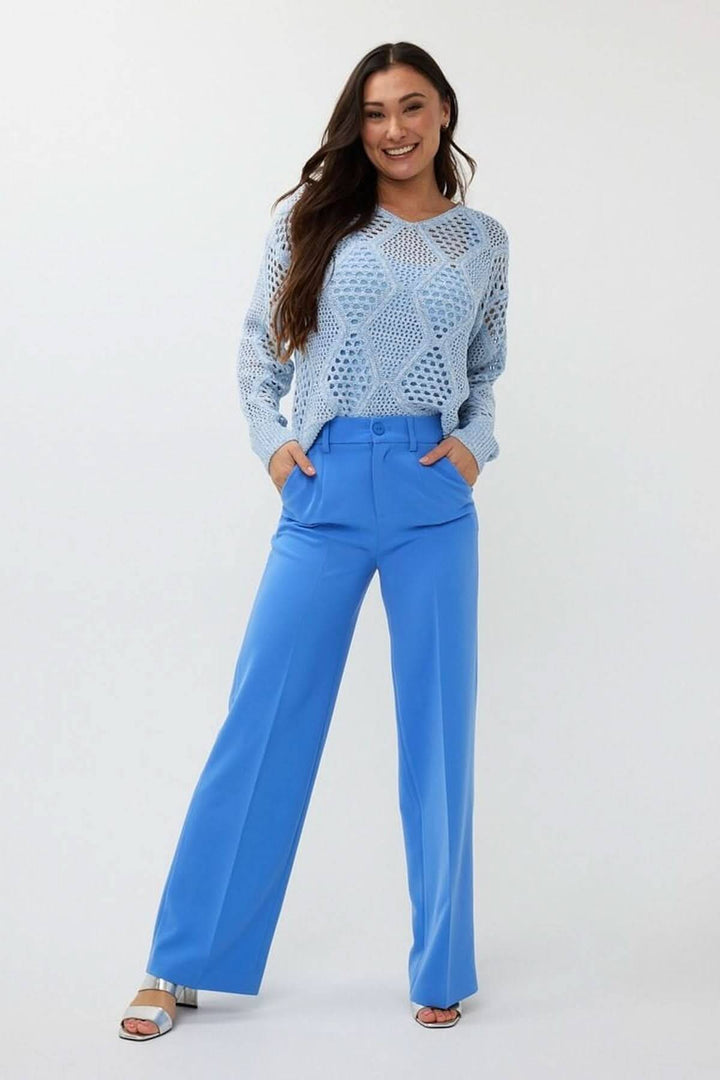 Femme portant un chandail en crochet ajouré bleu et un pantalon bleu, look chic et décontracté.