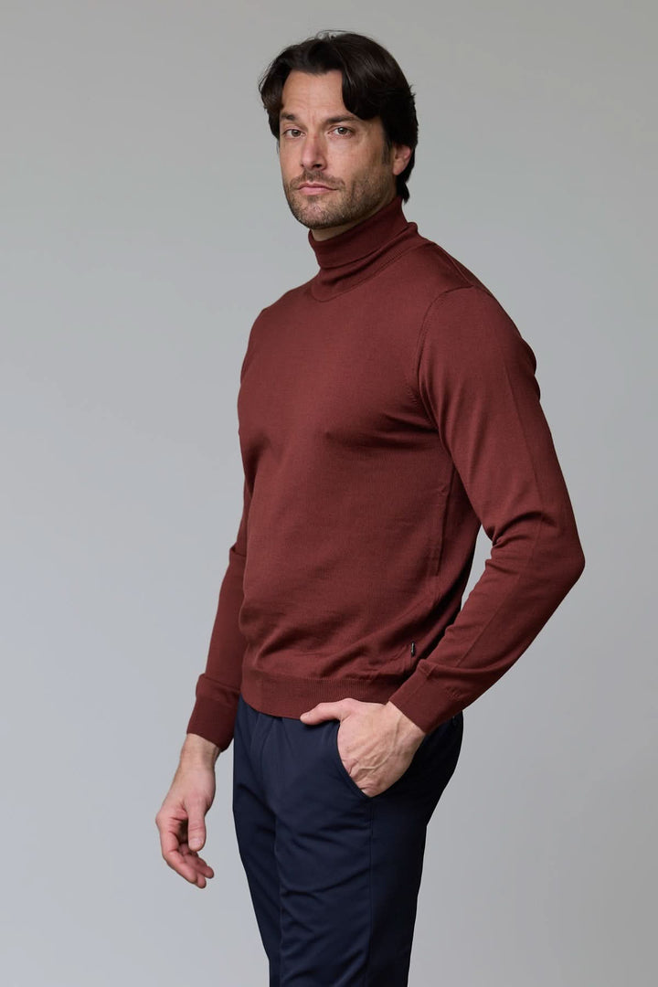 Homme portant un chandail en laine mérinos fine brun, à col roulé, avec un pantalon sombre, pour un style élégant et confortable.