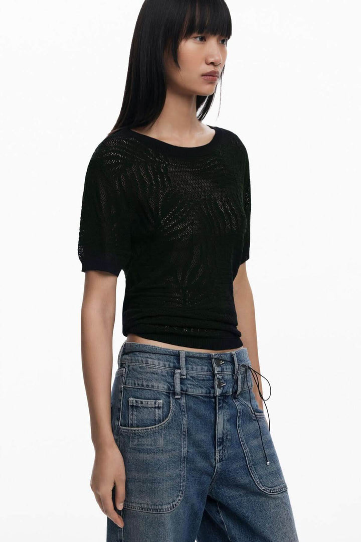 Chandail en maille ajourée noir avec col rond et manches courtes, porté avec des jeans décontractés.