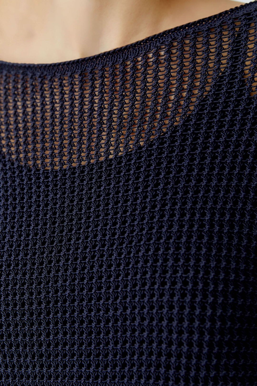 Gros plan sur le chandail en maille ajourée à manches longues, texture filet contraste avec la peau, soulignant l'encolure dégagée.