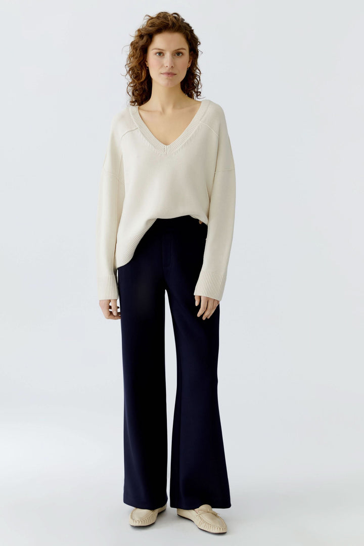 Femme portant un chandail en maille à col en V, élégant et confortable, assorti à un pantalon chic pour un look moderne et intemporel.