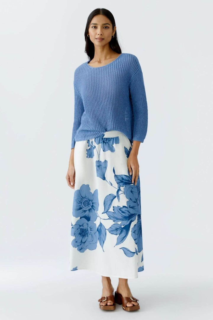 Femme portant un chandail en maille côtelée bleue avec une jupe fluide à fleurs blanches et bleues.