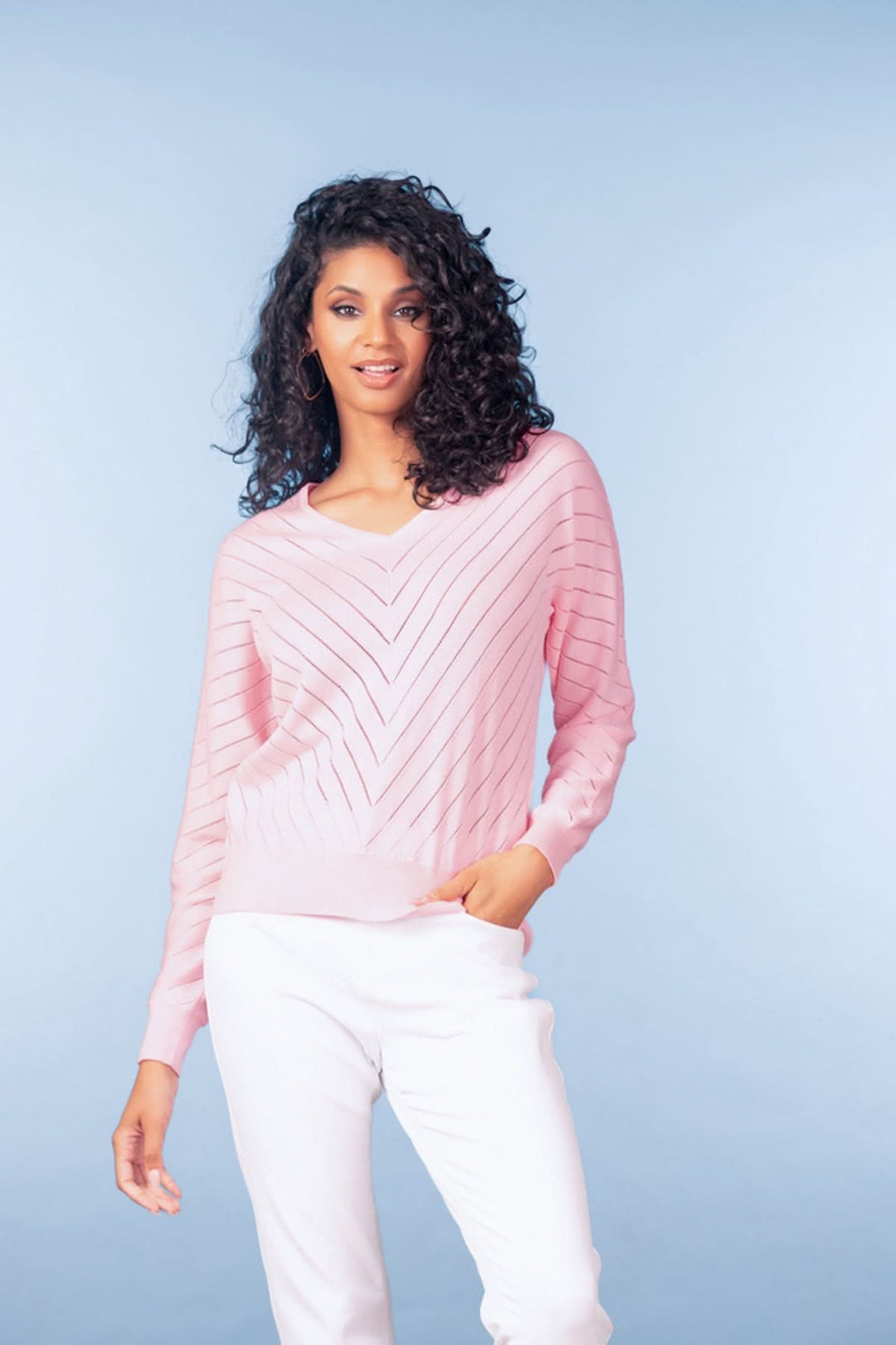 Femme portant un chandail en maille fine rose avec motif chevrons et encolure en V, ajoutant une élégance subtile à sa silhouette.