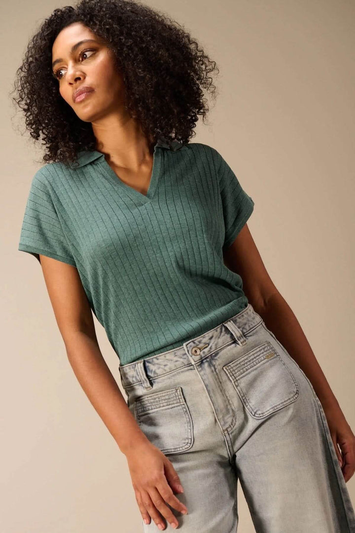 Femme portant un chandail en maille fine côtelé vert avec encolure en V et col polo, style moderne et polyvalent.