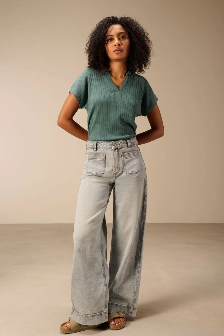 Femme portant un chandail en maille fine vert avec encolure en V et col polo, assorti à un jean large pour un look moderne et polyvalent.