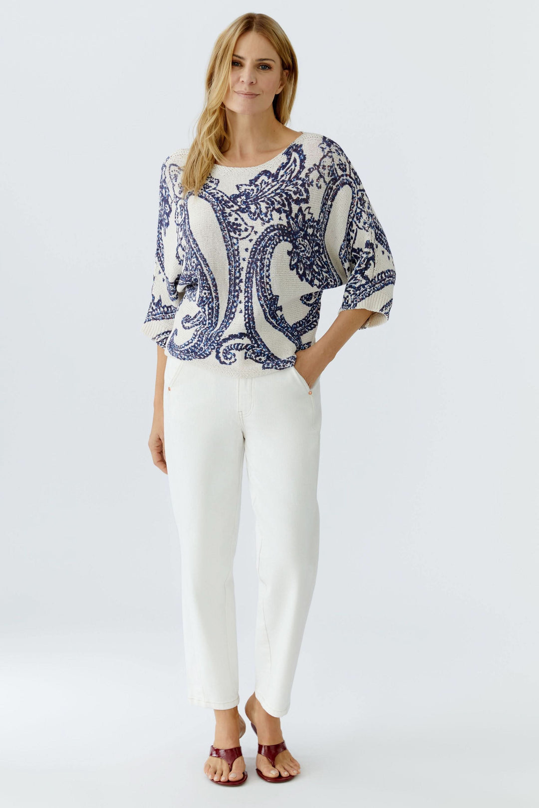 Femme portant un chandail en maille à motif cachemire avec manches trois-quarts et pantalon blanc, alliant style et confort.