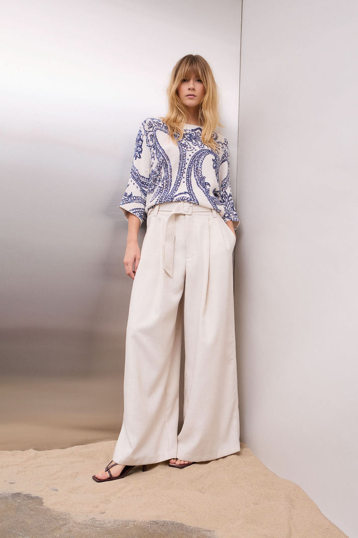 Femme portant un chandail en maille à motif cachemire avec des manches trois-quarts, associé à un pantalon ample sur fond neutre.