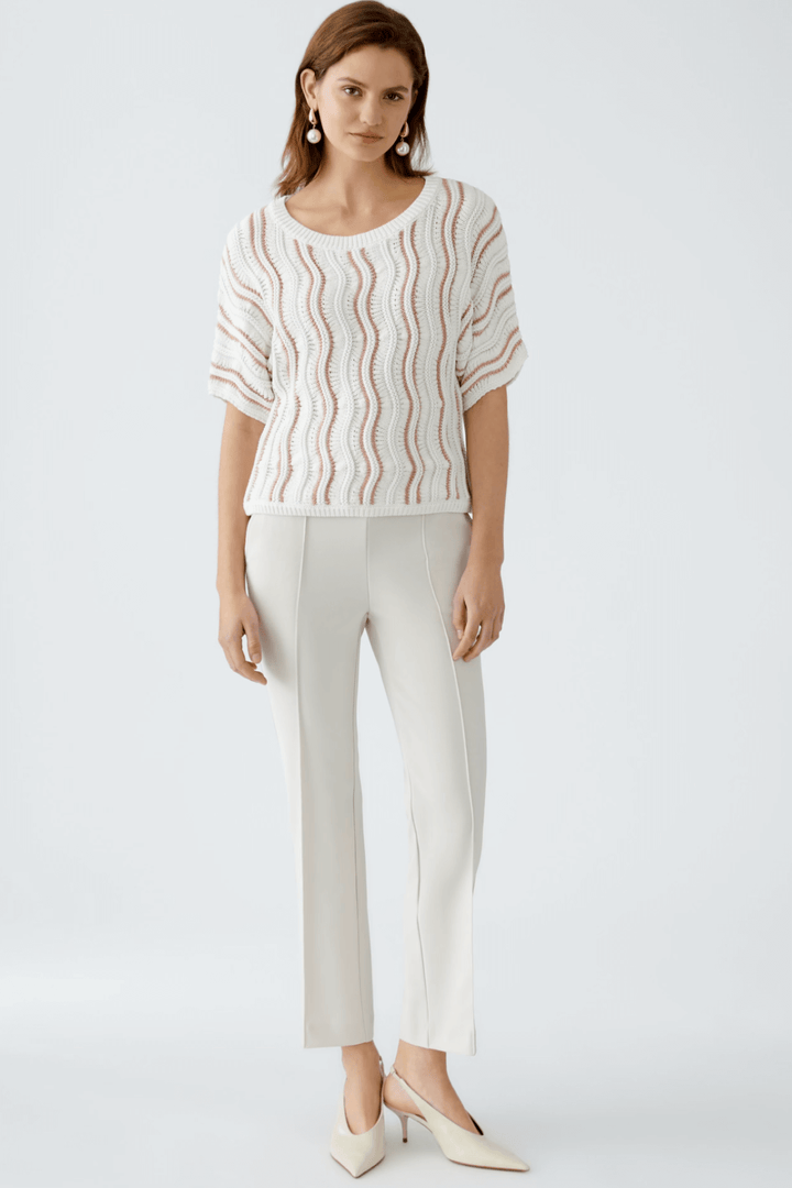 Femme portant un chandail en maille texturée à motif ondulé, associé à un pantalon clair et des chaussures élégantes.