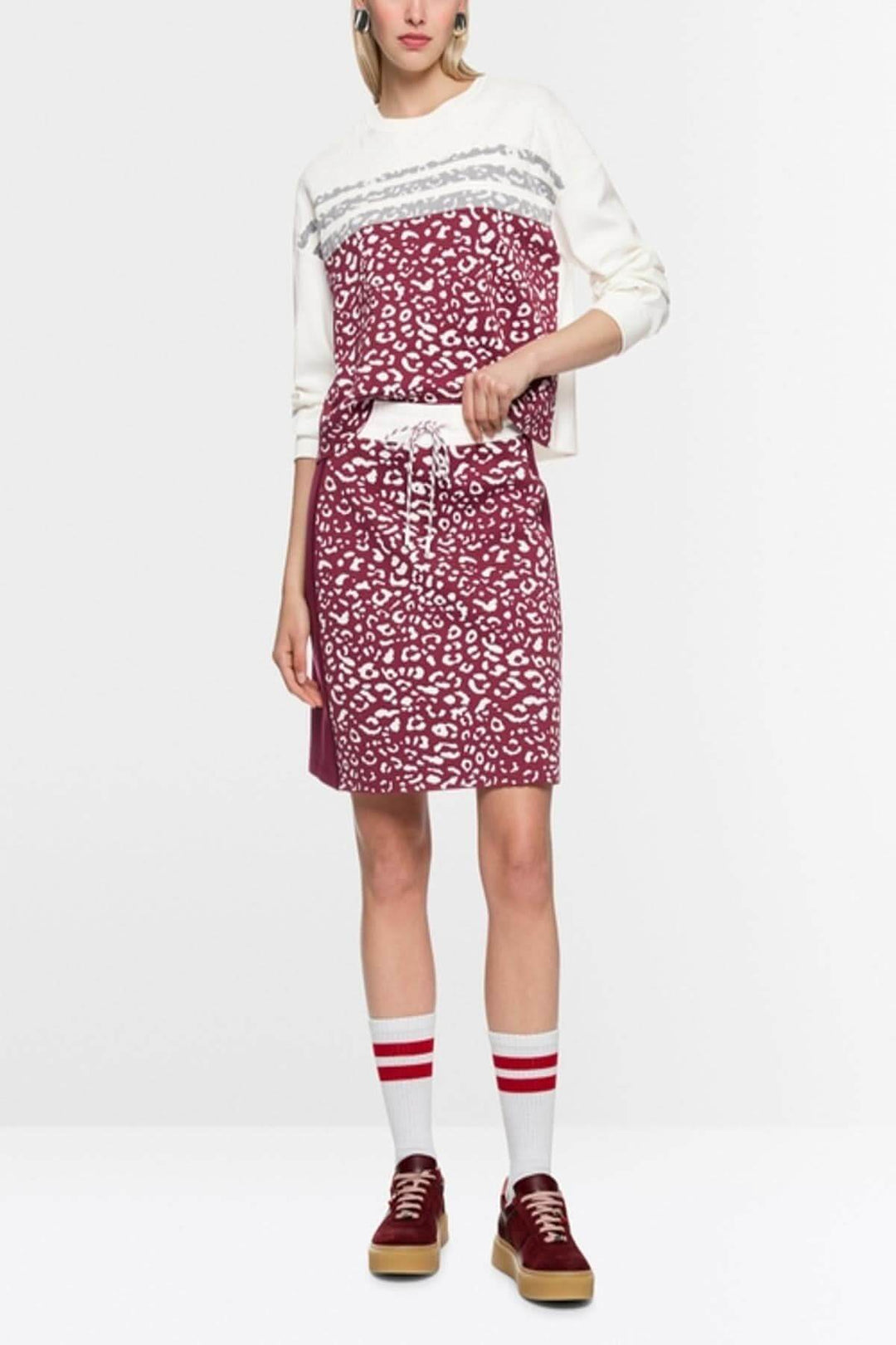 Chandail en tricot à imprimé graphique avec manches longues et col rond, porté par un mannequin avec jupe assortie et chaussures rouges.