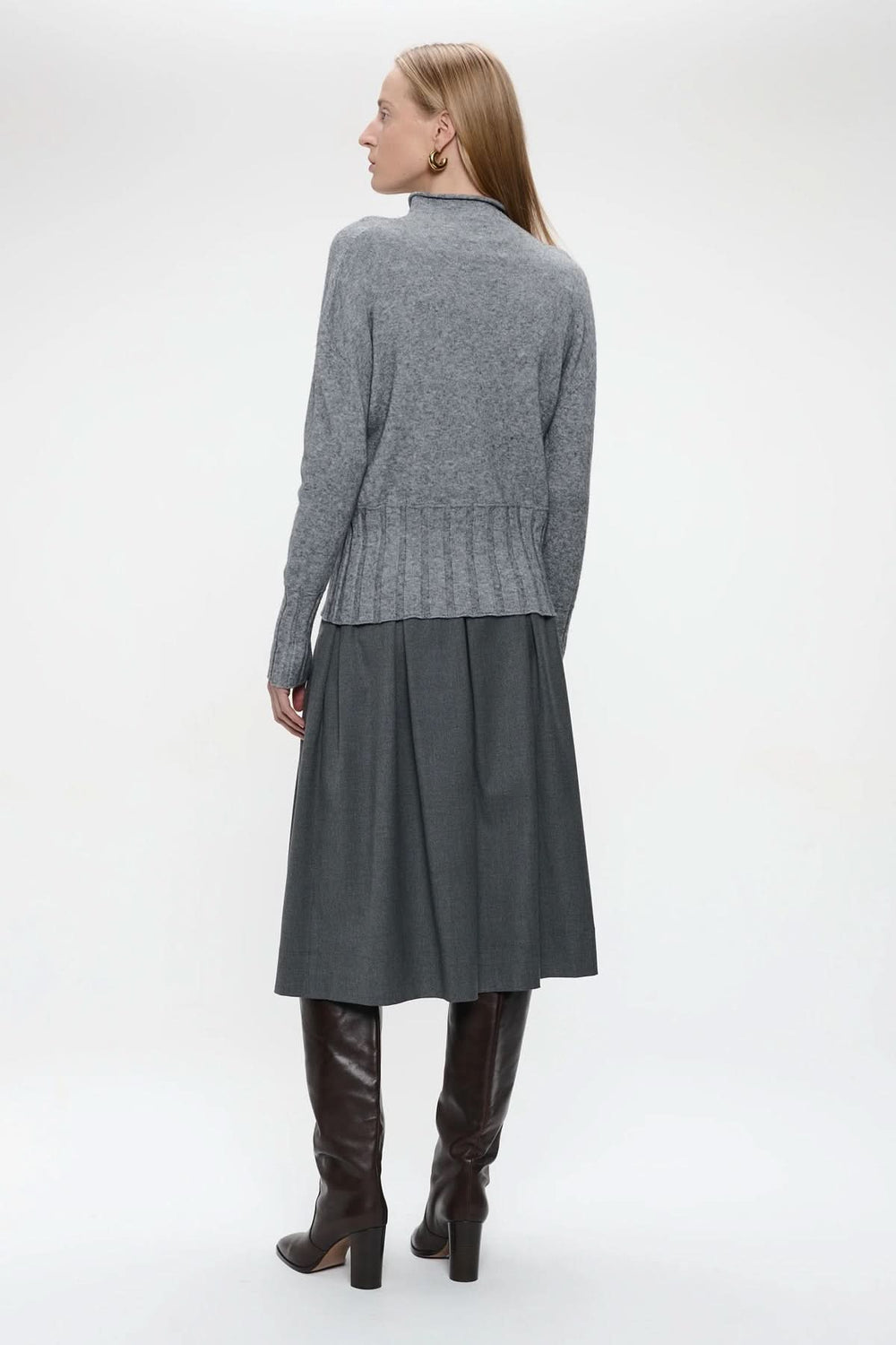 Femme portant un chandail en tricot gris avec une encolure montante et manches longues, jupe ample et bottes hautes. Décris moi le produit en français.