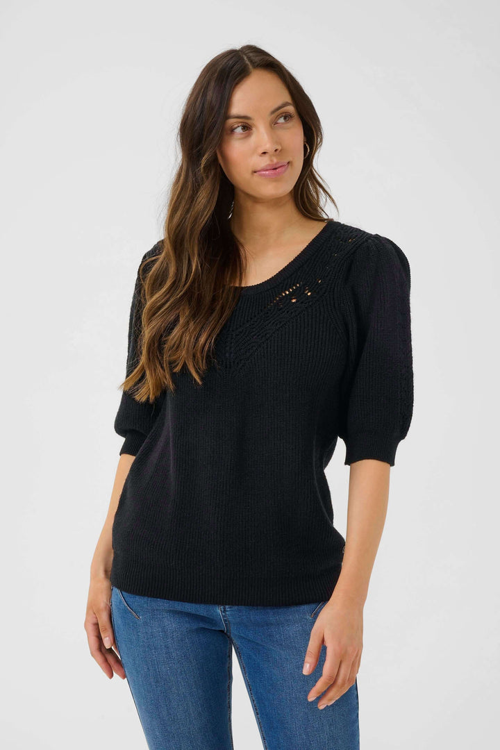 Chandail en tricot noir à manches bouffantes, motif ajouré sur le buste et encolure arrondie, look féminin et raffiné.