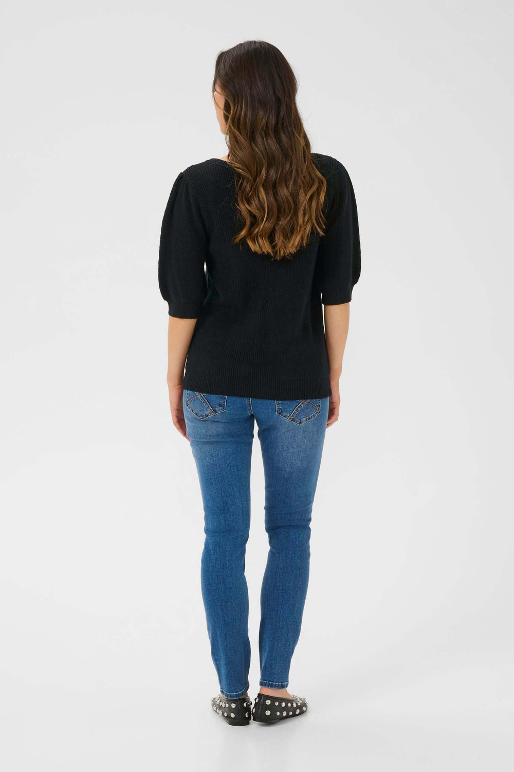 Femme portant un chandail en tricot noir avec manches bouffantes et jean, vue de dos.