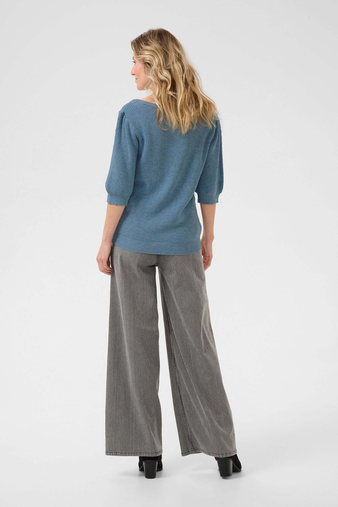 Femme vue de dos portant un chandail en tricot texturé bleu et un pantalon large gris.